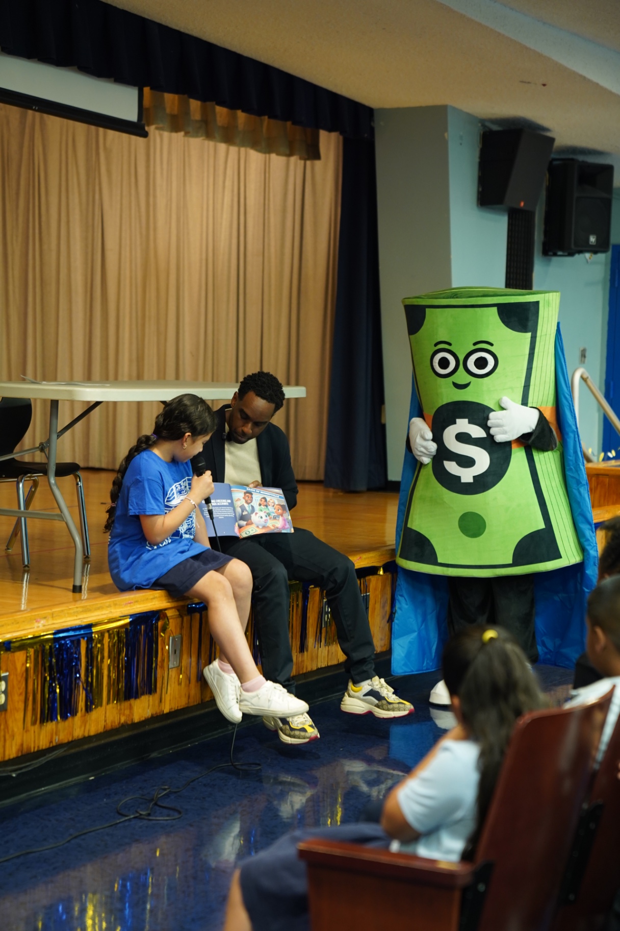 A student reading The Tales of Endless Rewards on stage beside Captain Cash